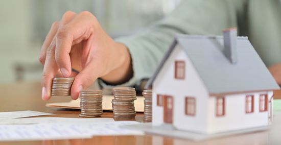 Man piling up coins against a model of a house as a concept of saving money.